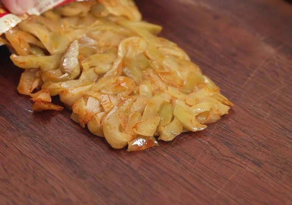 A packet of preserved mustard greens being poured onto a wooden cutting board, ready to be chopped.