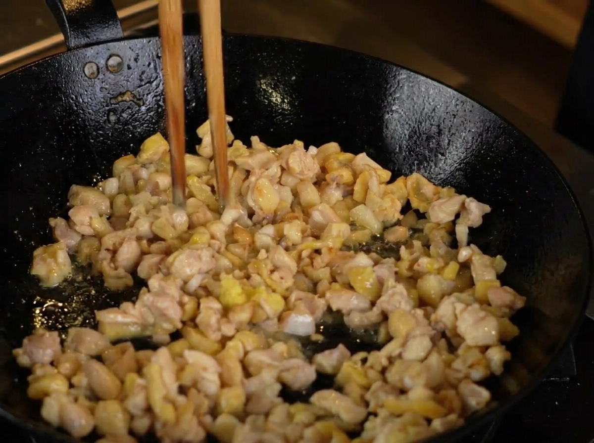 Grated ginger being added to chicken pieces browning in a hot pan.