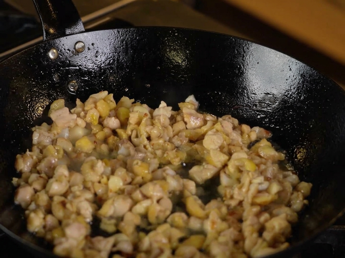Sake being poured into a pan containing chicken and aromatics.