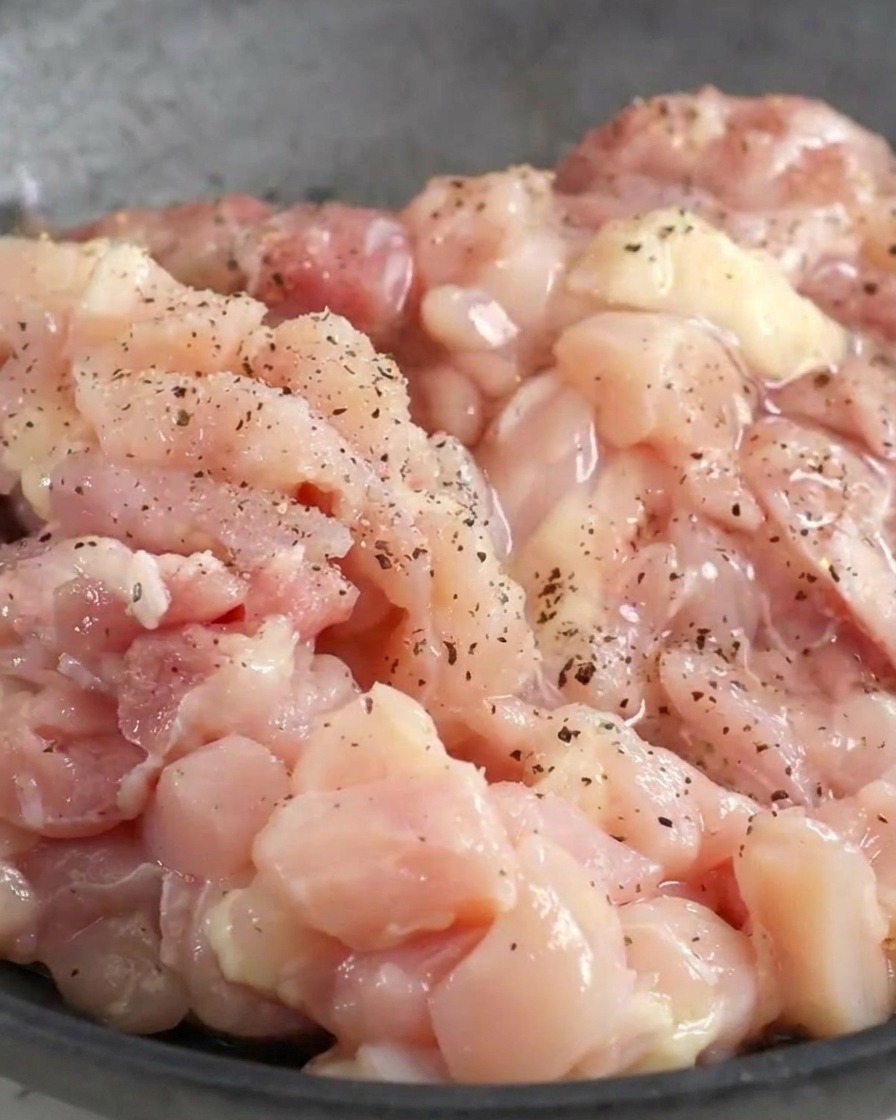 Chopped raw chicken in a bowl coated with black pepper and liquid seasonings.