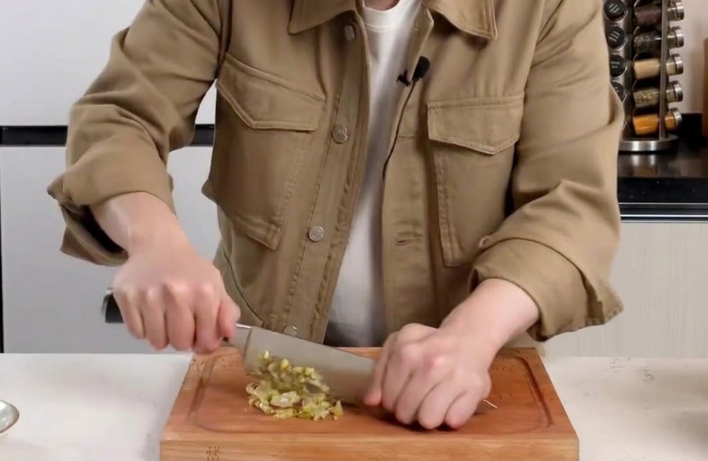 Finely dicing pickled mustard greens on a wooden cutting board with a knife.