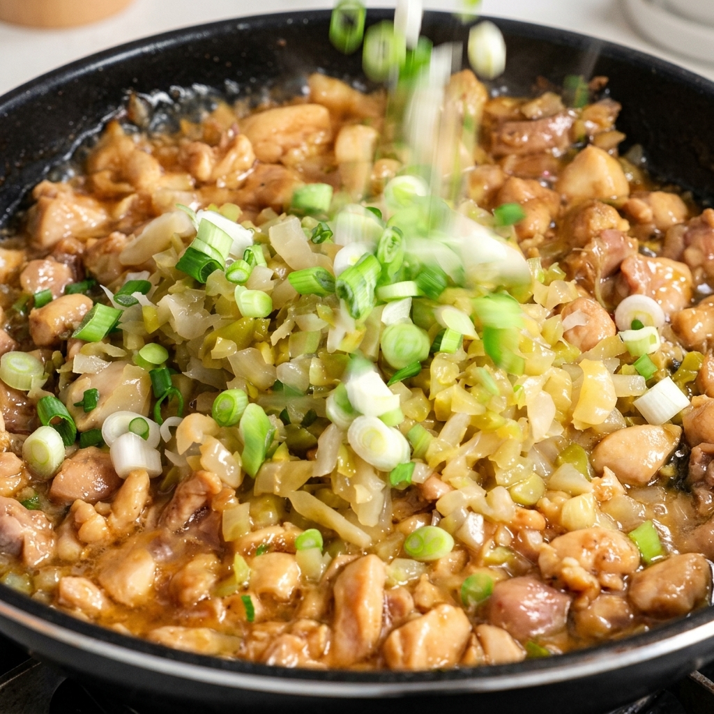 Chopped white parts of green onions being sprinkled into a skillet containing chicken and pickled greens.