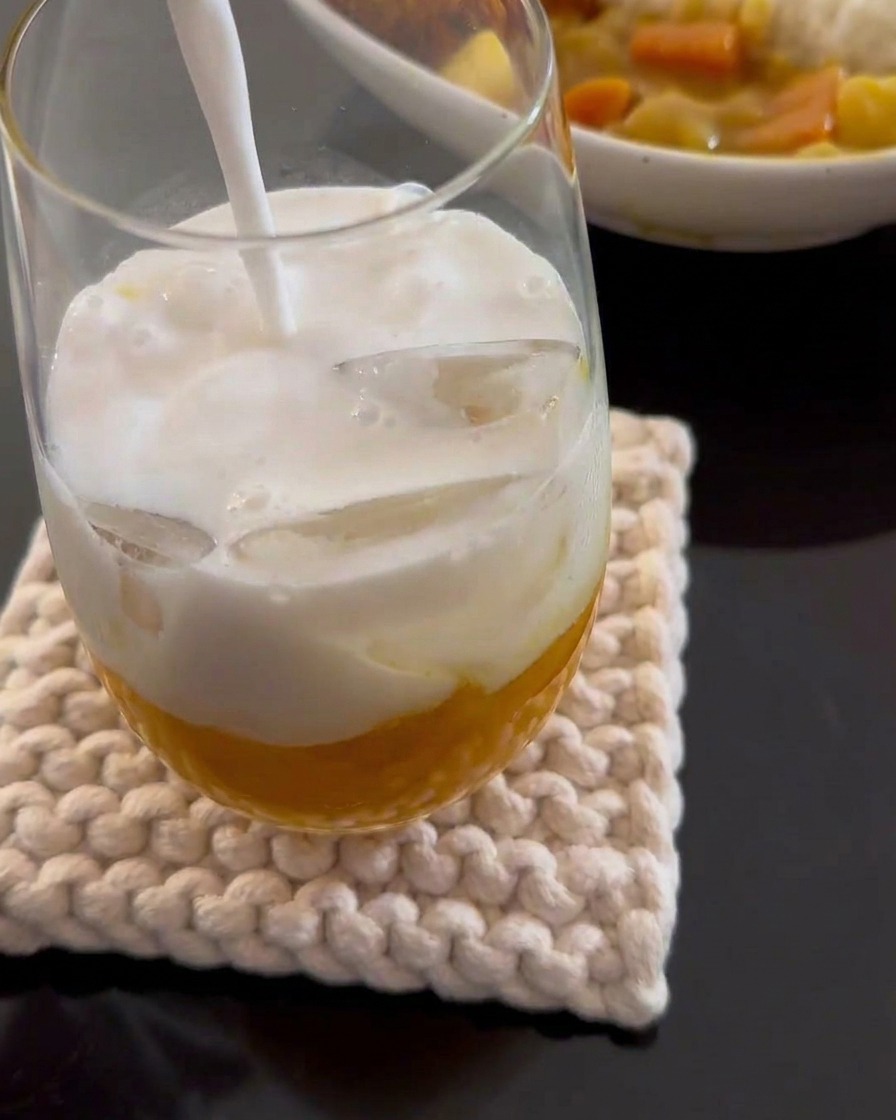 White coconut milk being poured into a tall glass containing yellow mango puree and ice cubes.