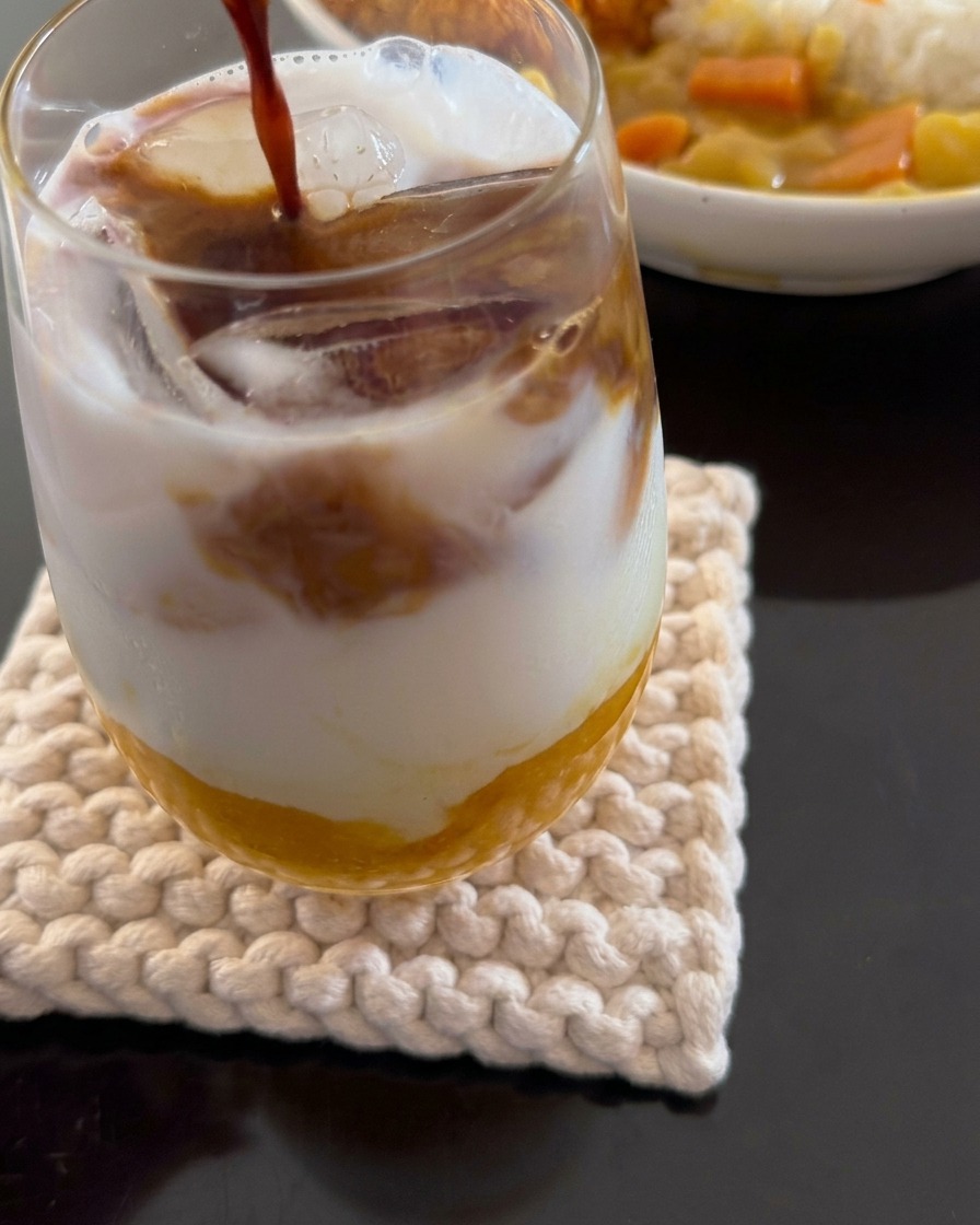 A close-up shot showing espresso being poured into a layered drink consisting of mango pulp, coconut milk, and ice.