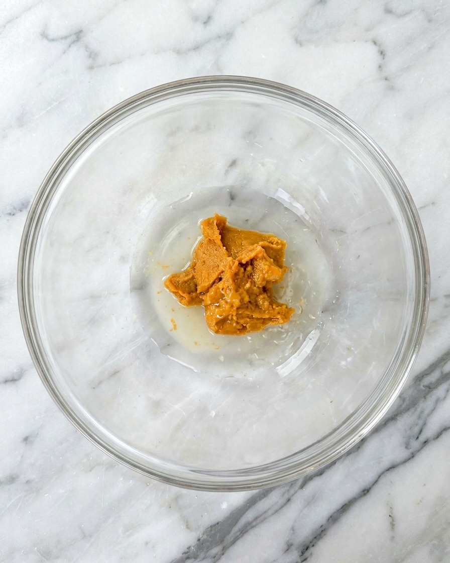 Mirin being poured into the glass bowl, joining the miso, sugar, and water.