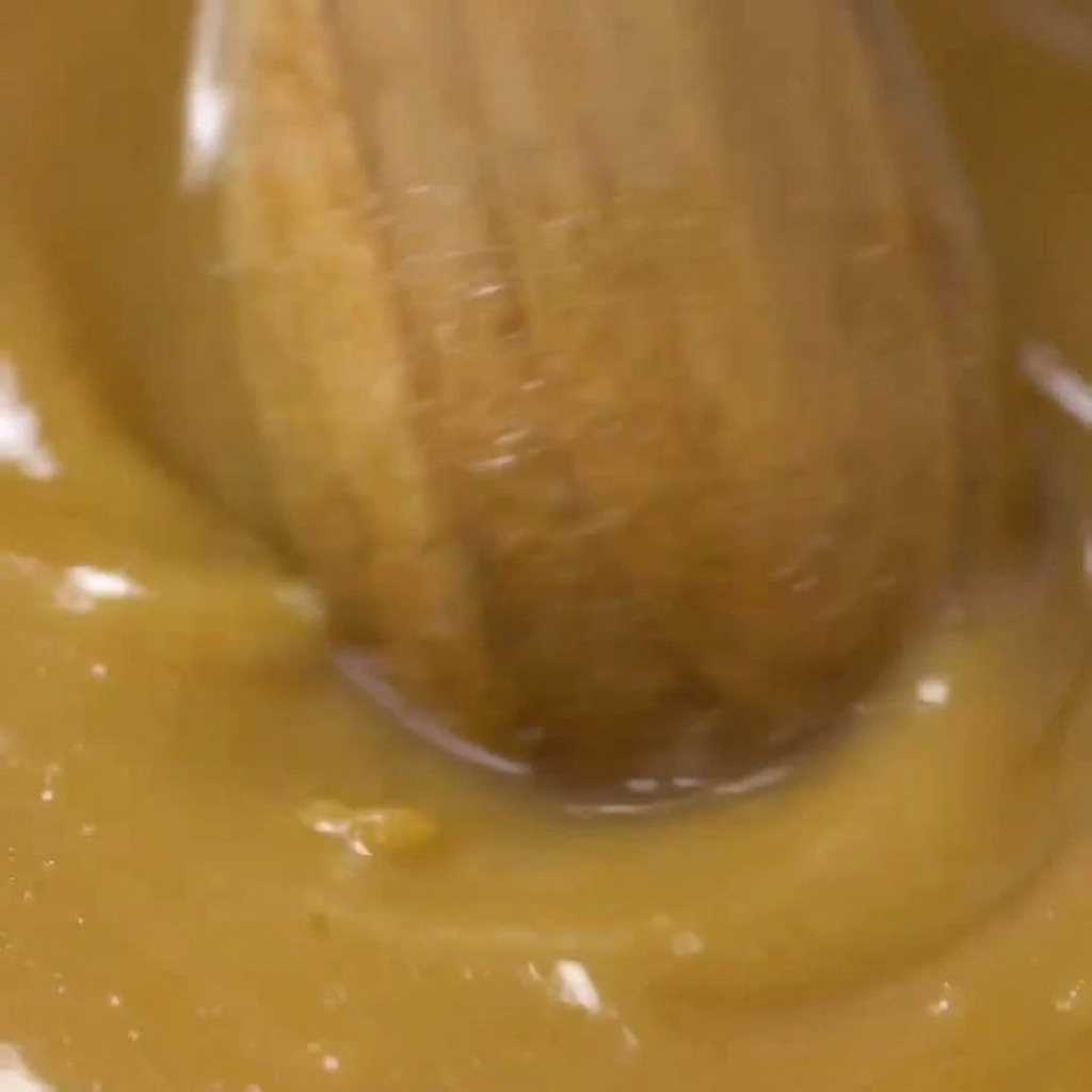 A wooden spoon stirring the golden-brown miso marinade in a glass bowl until the texture is uniform.