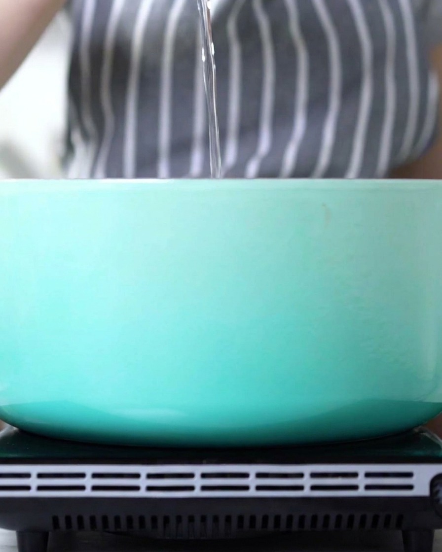 A thin stream of oil being poured into a clean, empty light blue enameled pot.