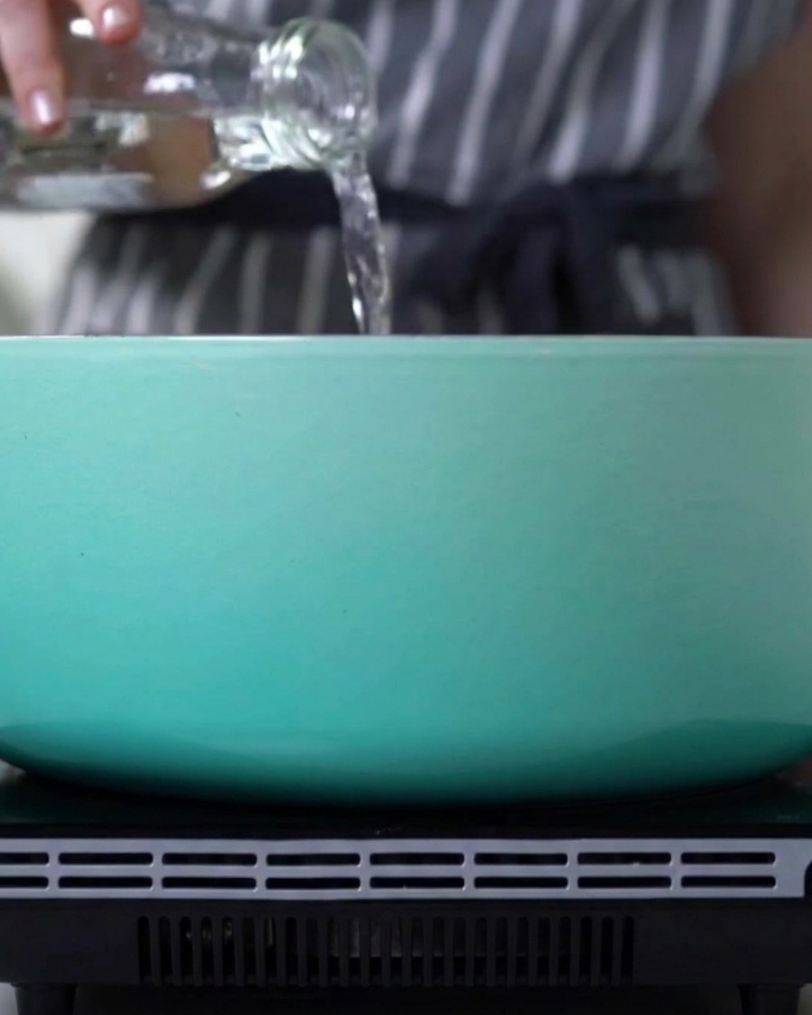 Water being poured from a glass bottle into a light blue pot on a stove.