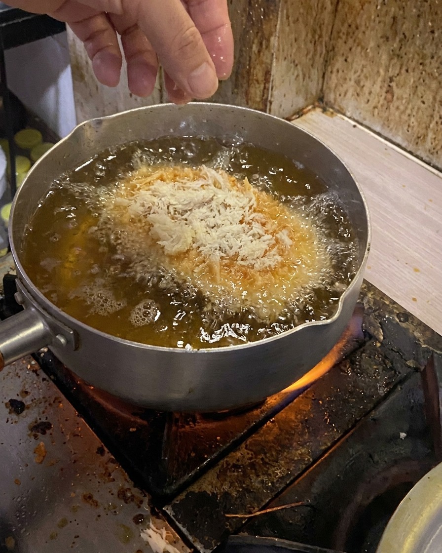 A breaded pork cutlet being gently lowered into a pot of bubbling hot oil.