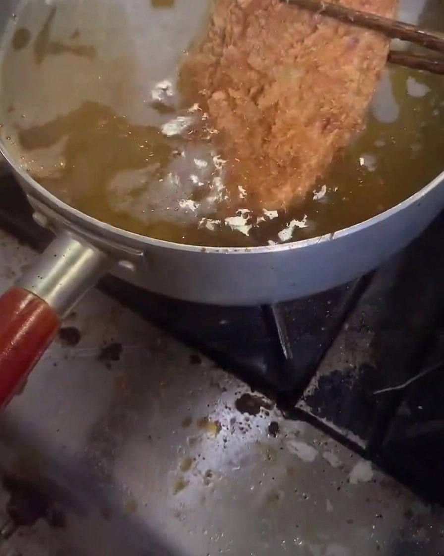A pork cutlet being deep-fried for the second time in hot, bubbling oil.