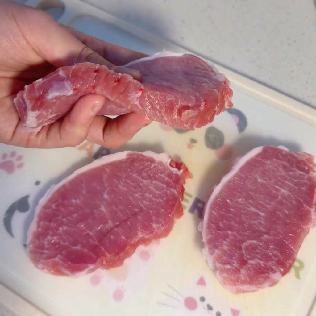 Thick slices of raw pork tenderloin resting on a cutting board.