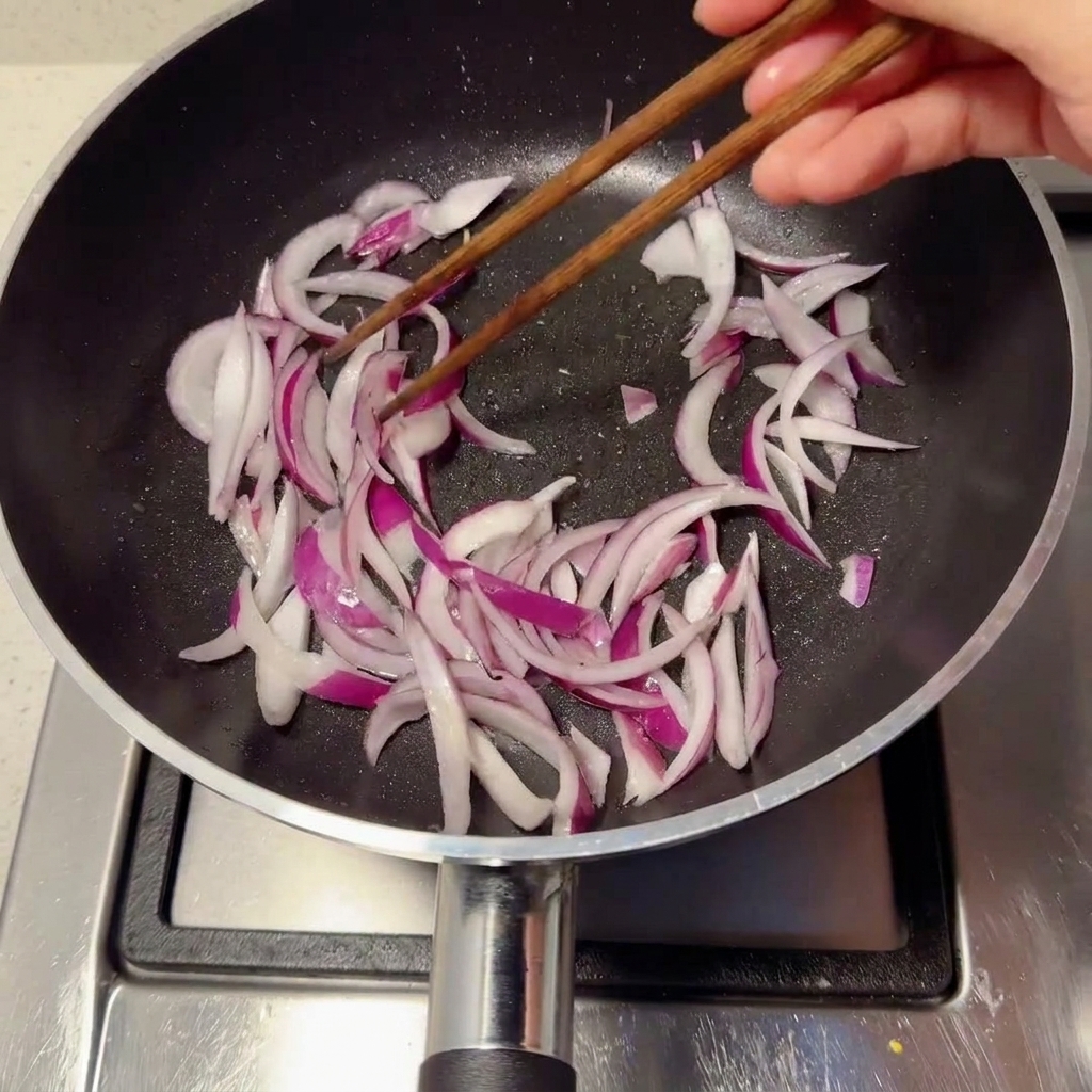 Sliced purple onions being tossed and stir-fried in a black pan using wooden chopsticks.