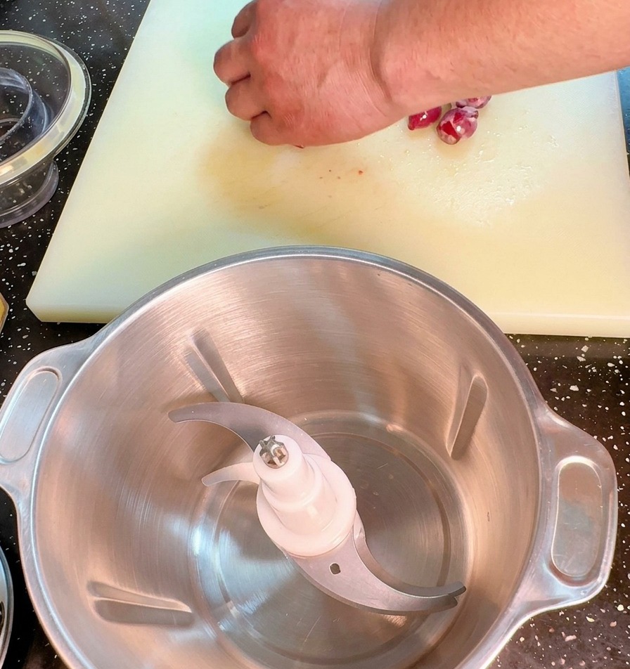 A close-up shot of a hand using a large kitchen cleaver to finely dice a red onion on a white plastic cutting board.