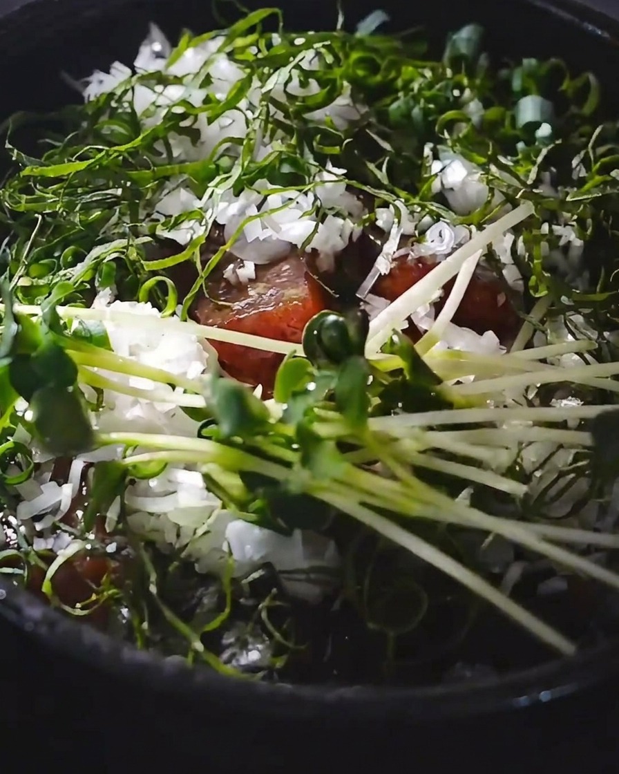 A raw egg yolk being added to the center of a garnished tuna rice bowl.
