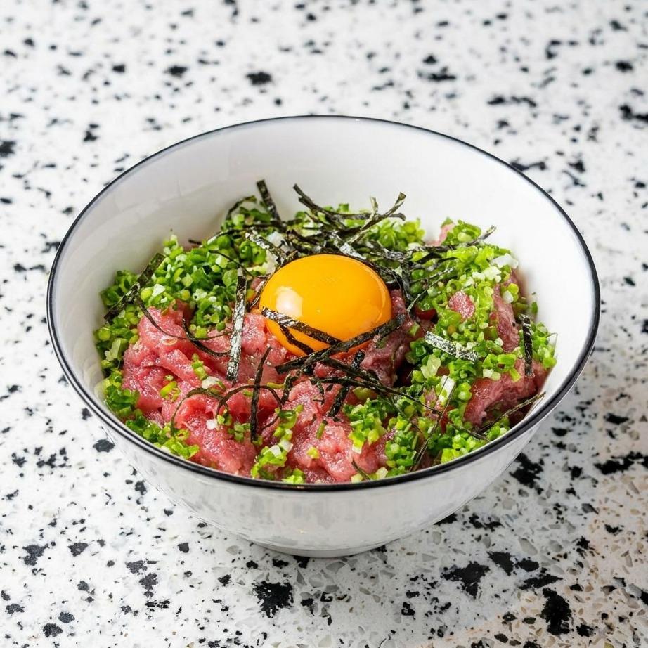 A bowl containing minced tuna and rice, topped with fresh scallions, shredded seaweed, and a raw egg yolk in the center.