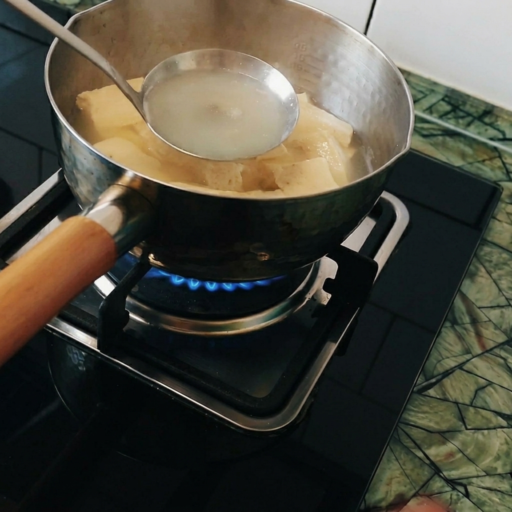 Curry pieces being dissolved in a ladle held inside the pot of boiling water.