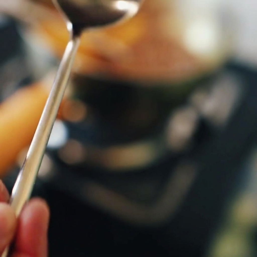 A spoonful of thick red chili paste being stirred into a simmering pot.