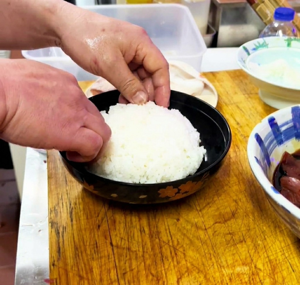 Cooked white rice being gently shaped and leveled inside a black serving bowl.