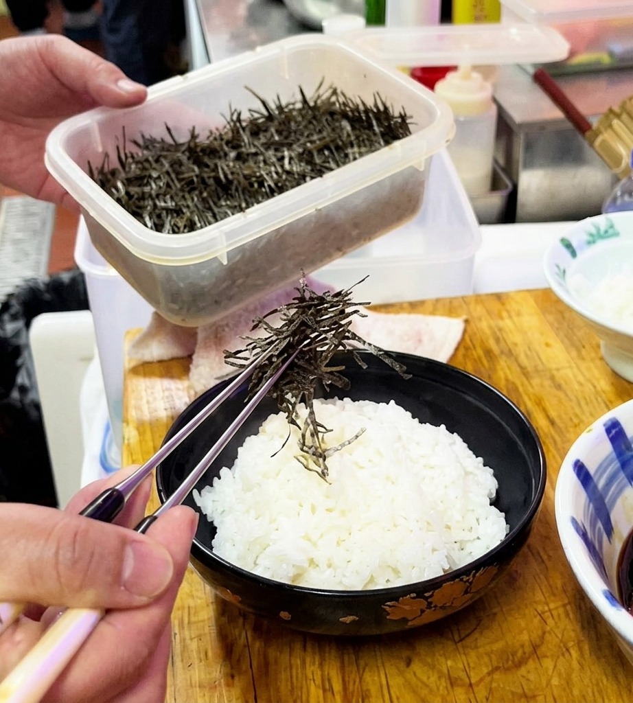 Shredded dried seaweed being sprinkled over a bowl of steamed white rice.