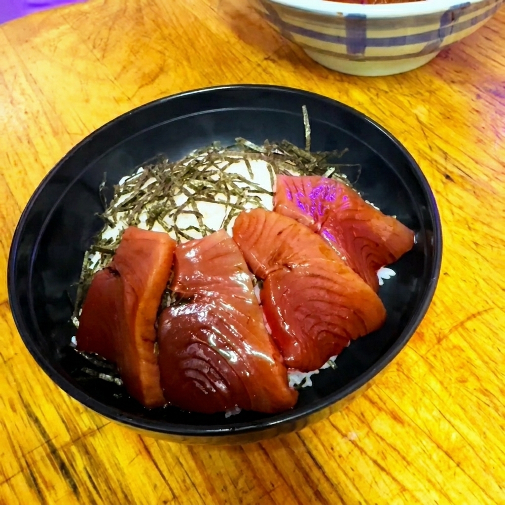 Marinated red tuna slices arranged in a neat, circular overlapping pattern inside a black bowl over rice.