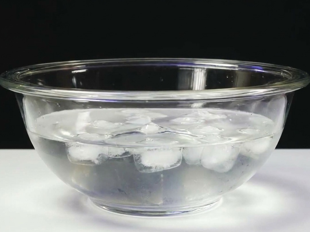A block of tuna submerged in a glass bowl filled with cold ice water.