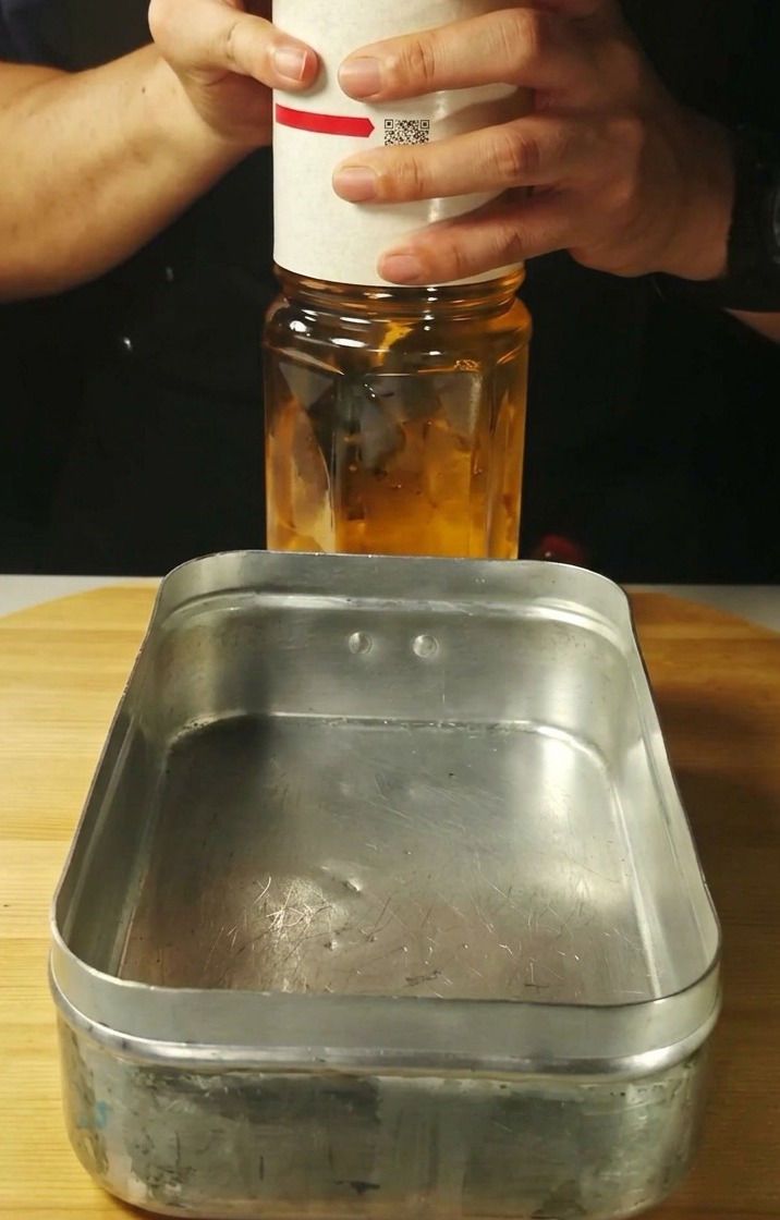Clear liquid being poured into a rectangular metal tray.