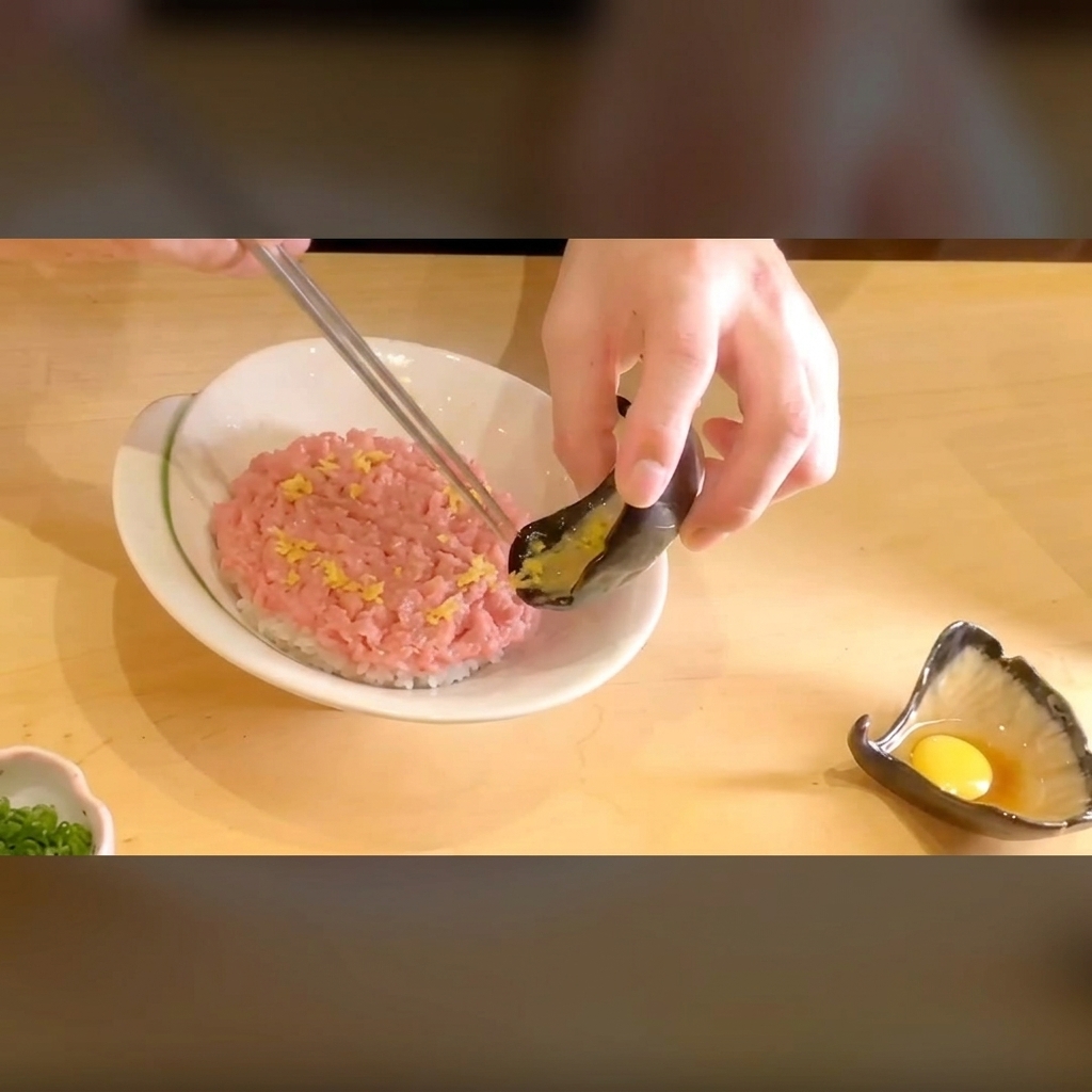 A close-up view of vibrant pickled yellow radish being placed onto a bed of minced tuna over rice.