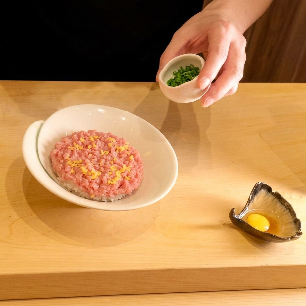 A hand sprinkling freshly chopped green onions from a small bowl over a layer of minced raw tuna.
