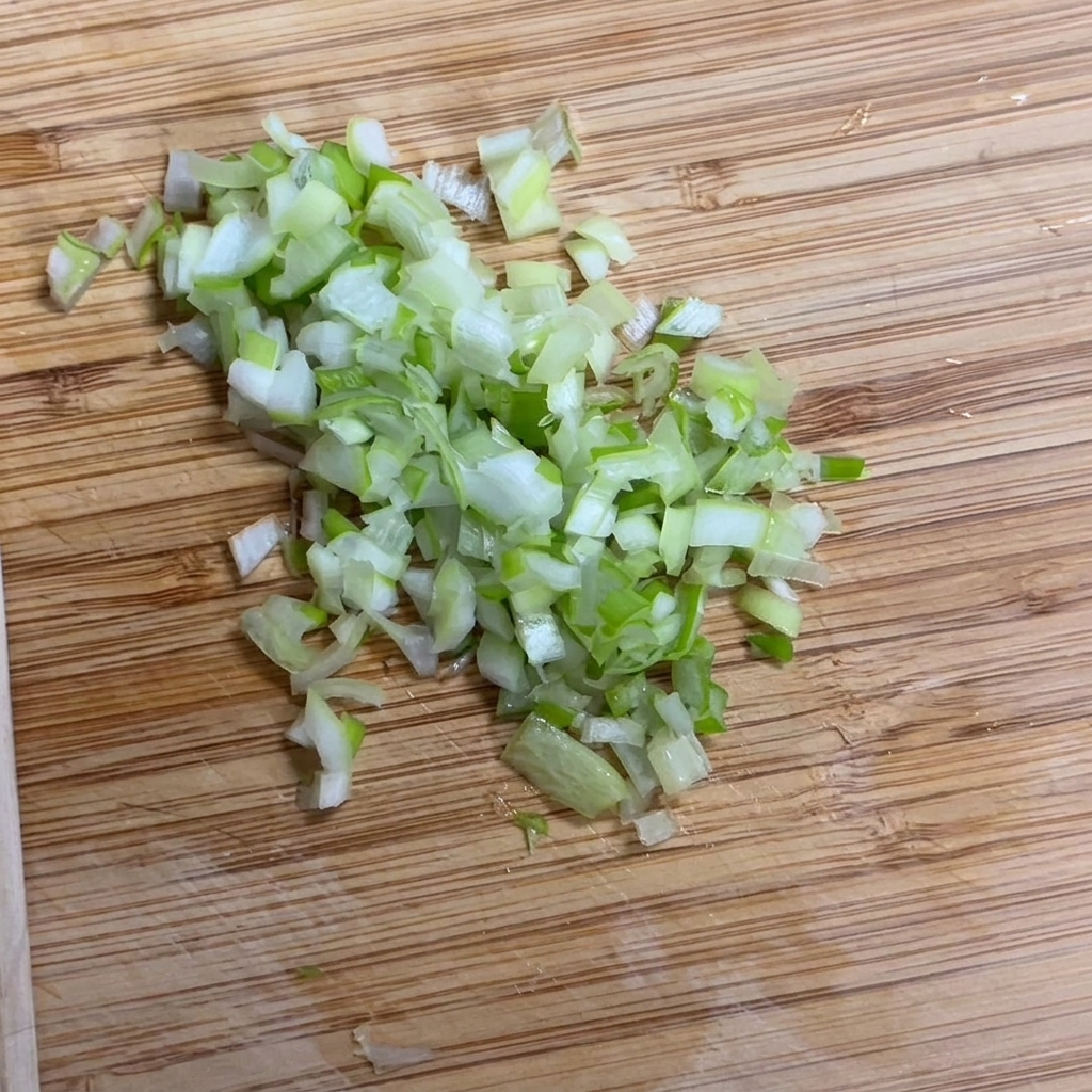 Fresh scallions being finely chopped on a wooden surface.