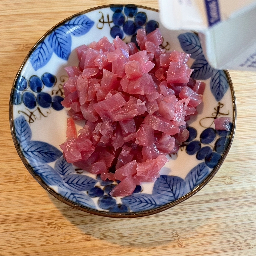 Soy sauce being drizzled over cubed tuna in a decorative bowl.