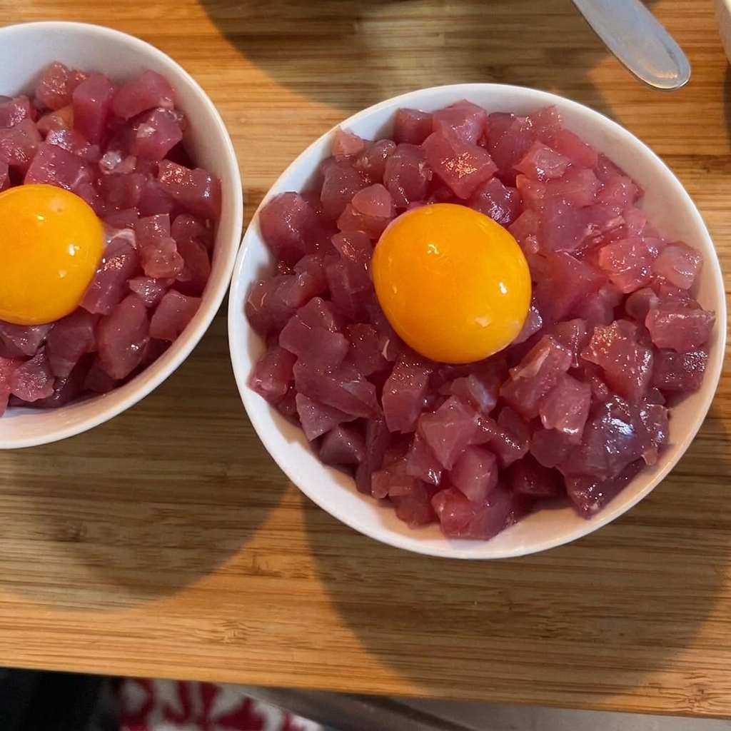 A vibrant, golden raw egg yolk sitting atop a bowl of tuna and rice, garnished with green scallions.