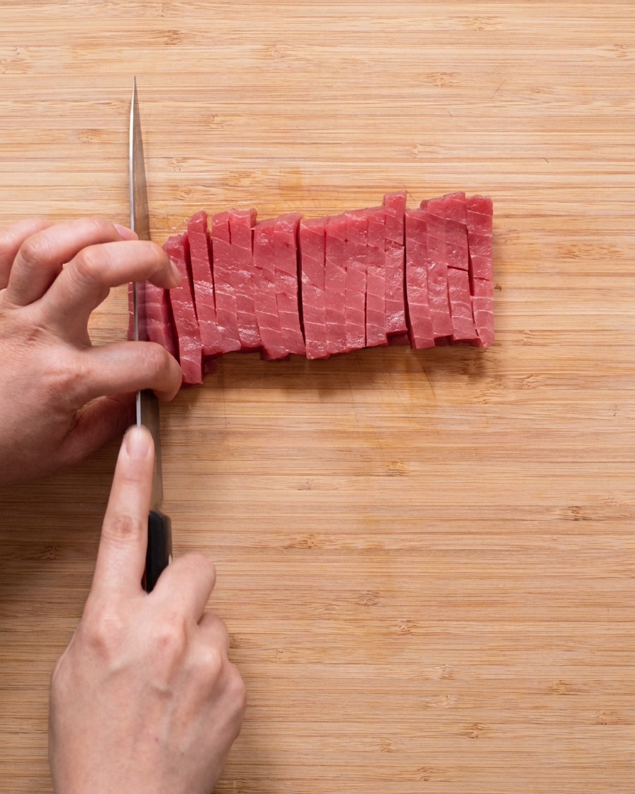 Uniform cubes of raw red tuna arranged on a wooden cutting board.