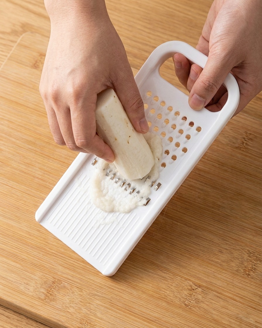 Freshly grated white Chinese yam paste being collected from a plastic grater.