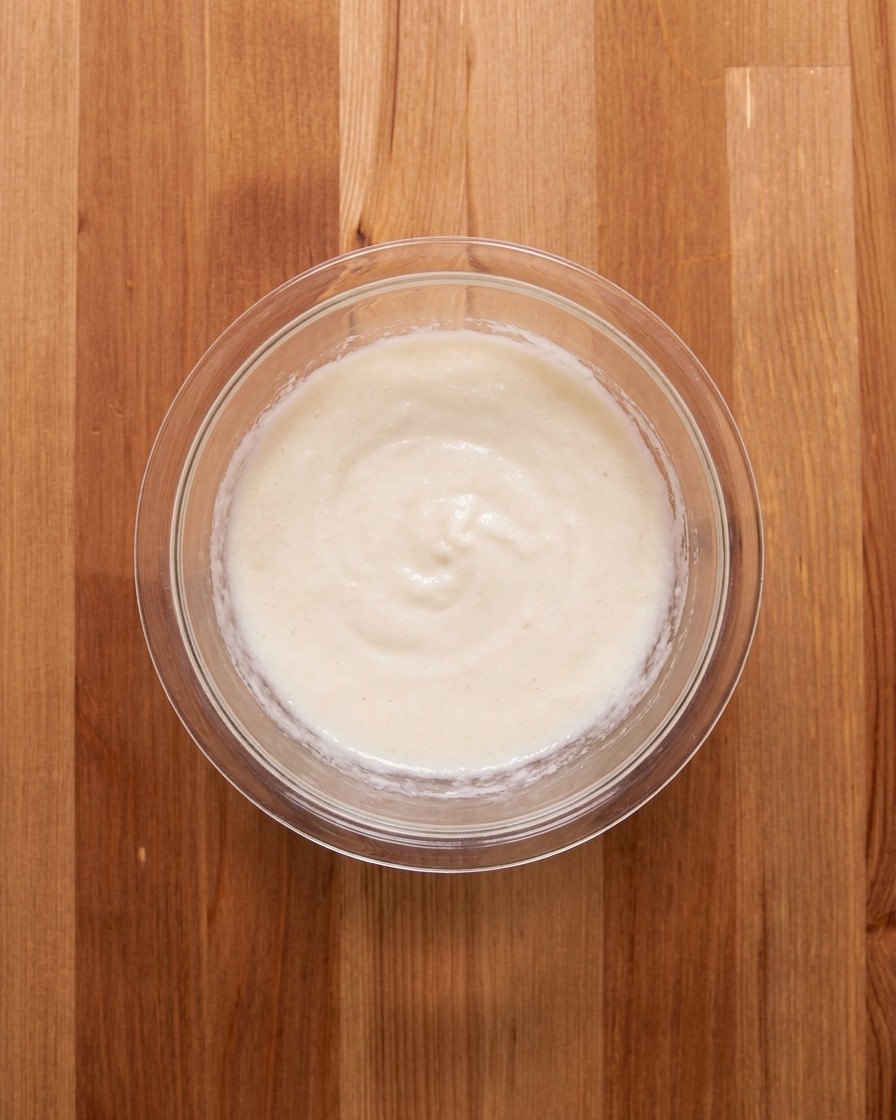 The white yam paste and meat broth being stirred together in a glass bowl.