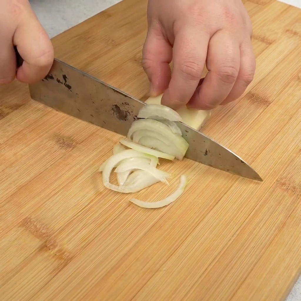 Thinly sliced white onion strips laid out on a wooden cutting board.