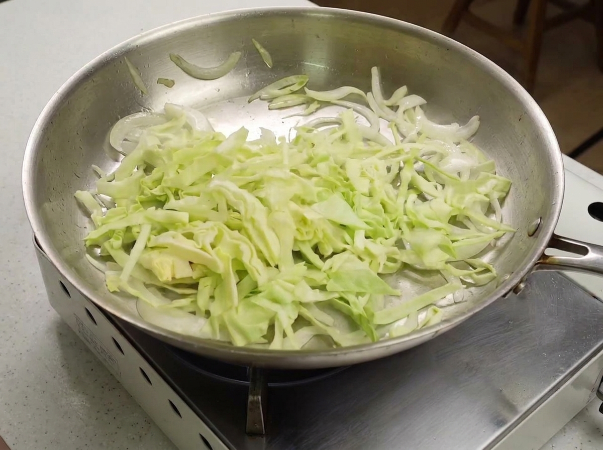 Finely shredded green cabbage added to a pan with lightly sautéed white onions.
