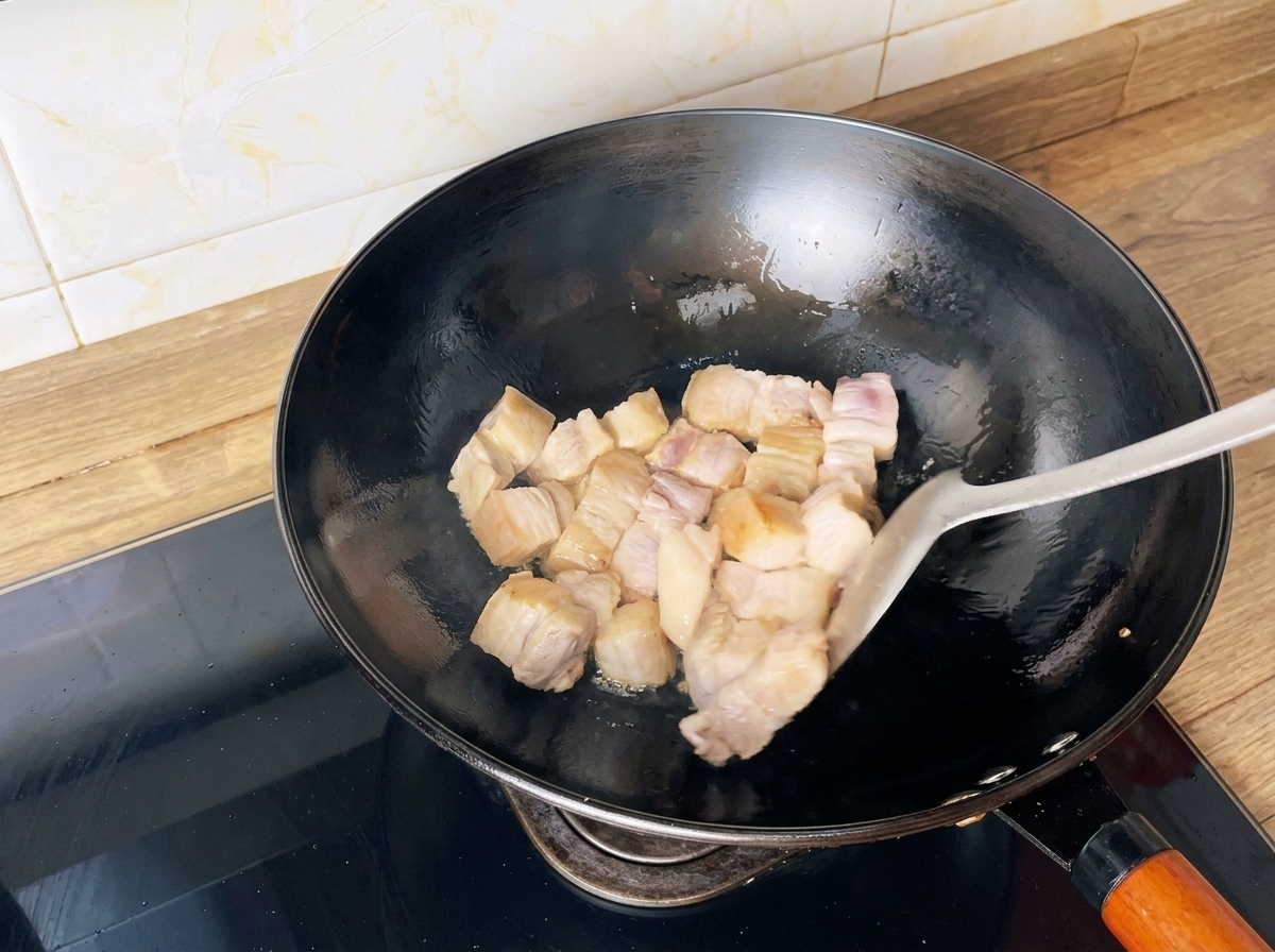 Pork belly cubes being stir-fried in a wok with a spatula until golden brown.
