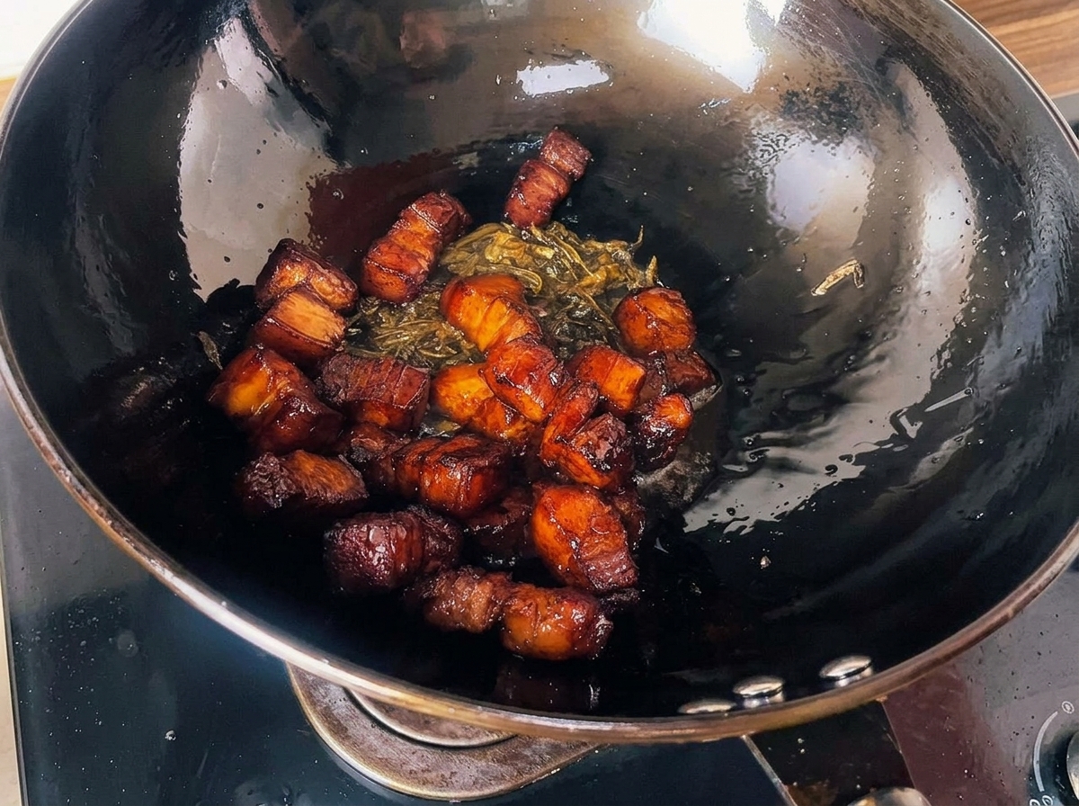 Roasted, dark glazed pork belly cubes mixed with crispy fried tea leaves resting inside a large black wok.