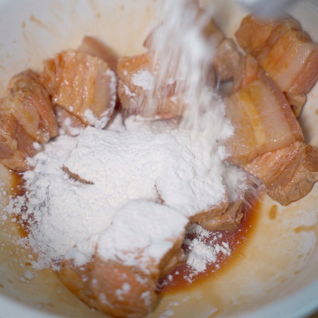 Pale pork slices in a bowl being dusted with a heavy layer of white tapioca starch.