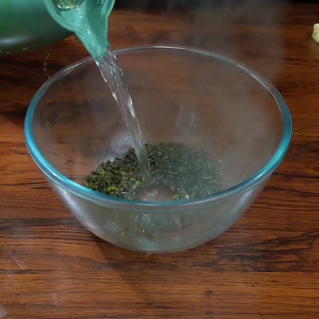 Pouring boiling water from a green kettle over Tieguanyin tea leaves in a clear glass bowl.