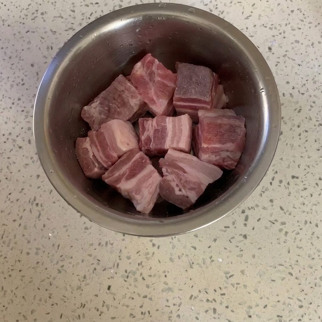Pork belly cubes in a metal bowl lightly coated with granulated sugar.