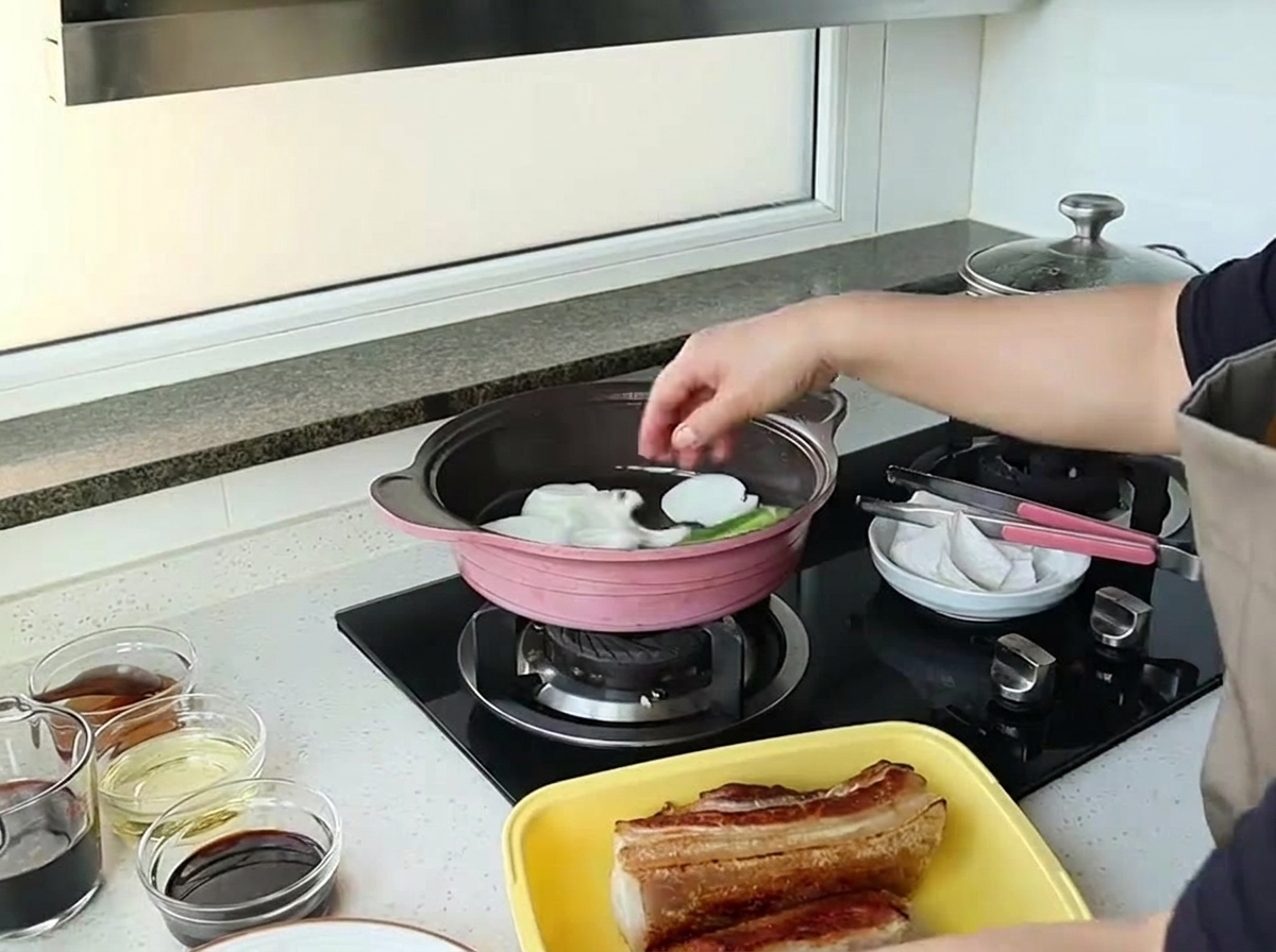 A hand dropping large chunks of white onion into a pink pan to sauté.