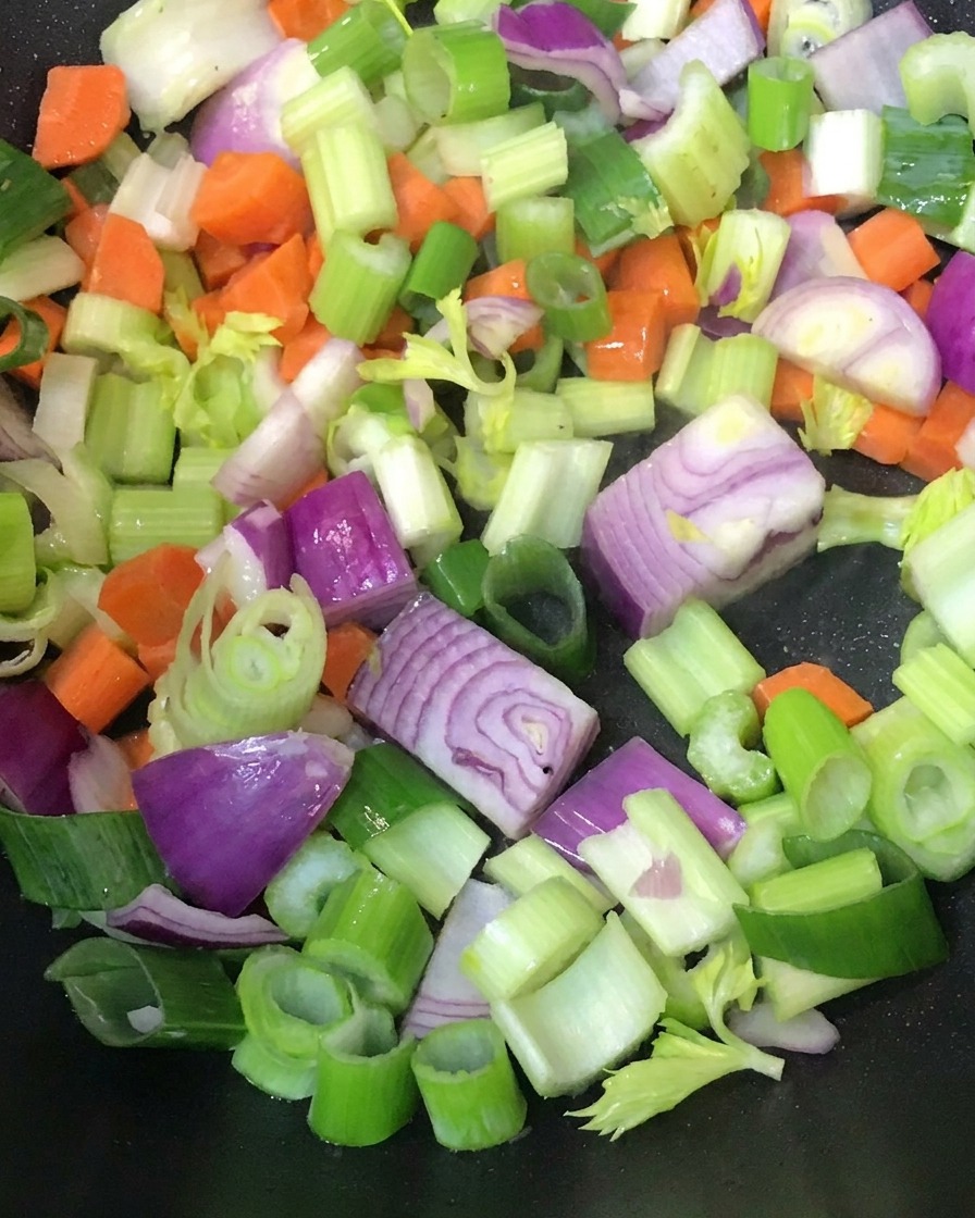 Diced vegetables being stir-fried in a hot pan.