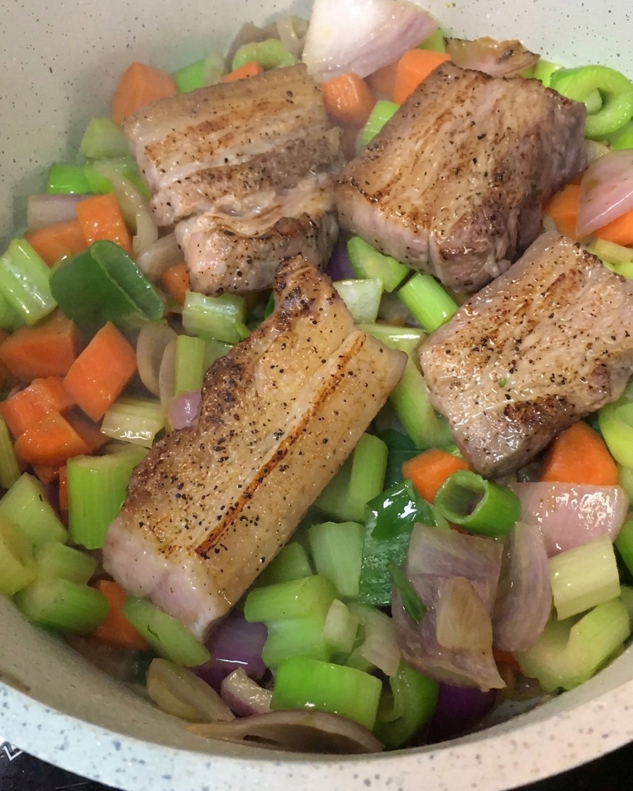 Seared pork belly pieces placed over a bed of sautéed vegetables in a cooking pot.