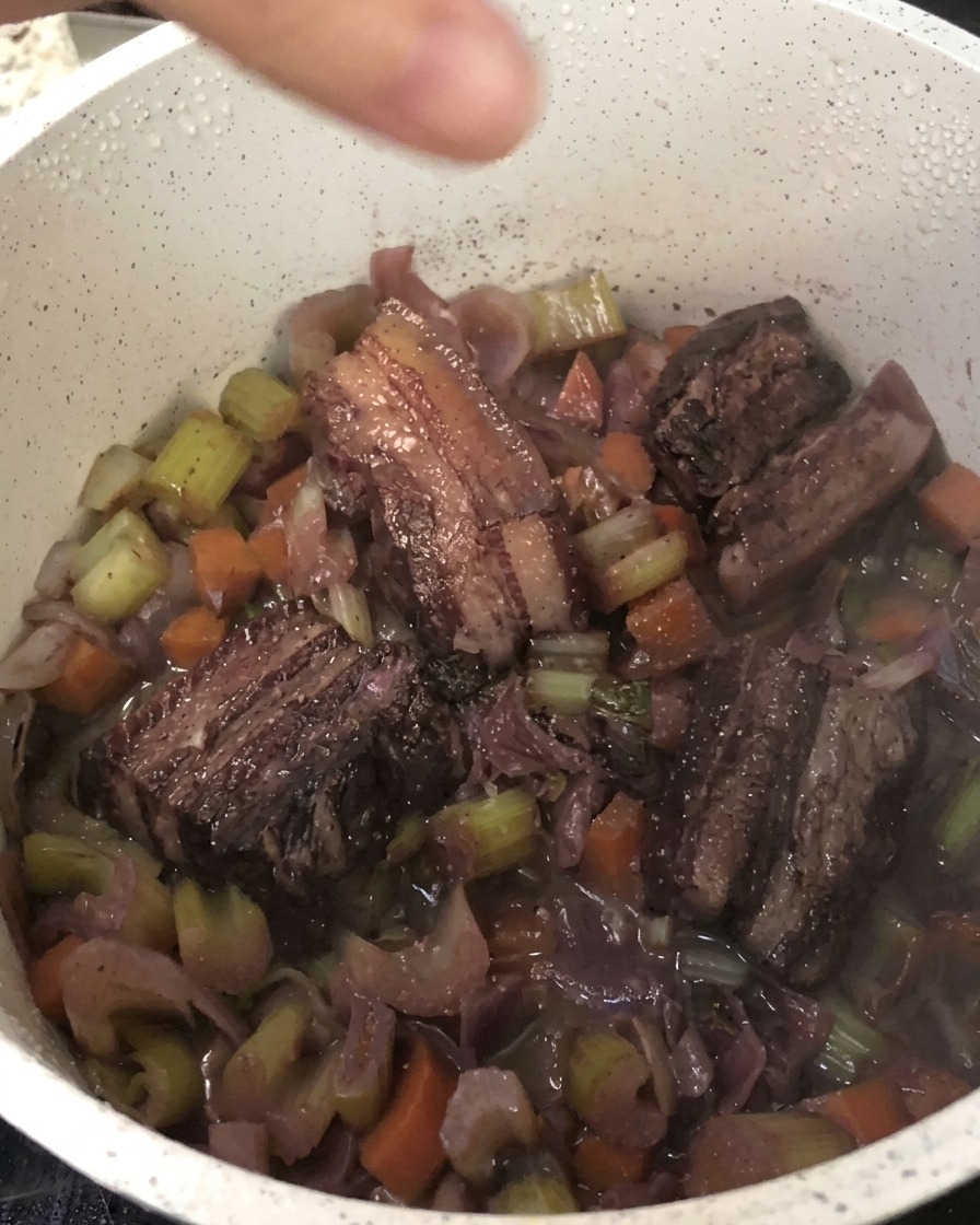 Fresh black pepper being ground directly into the pot of braised pork belly and vegetables.