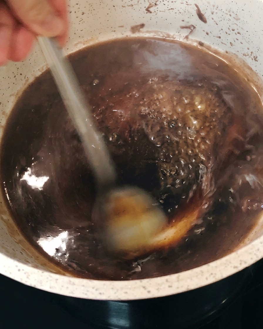 The dark red wine reduction bubbling and thickening in the pot while being stirred.