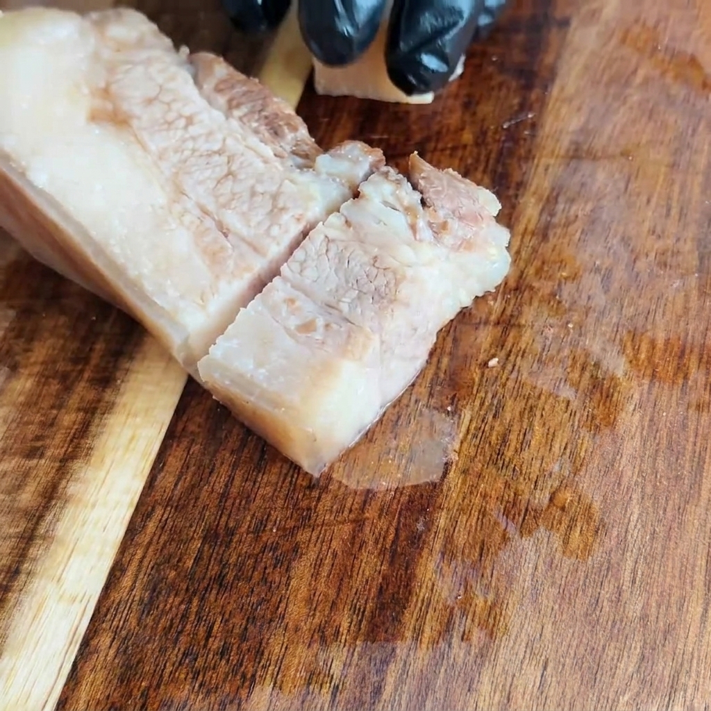 Cooled pork belly being sliced into even squares on a wooden cutting board.