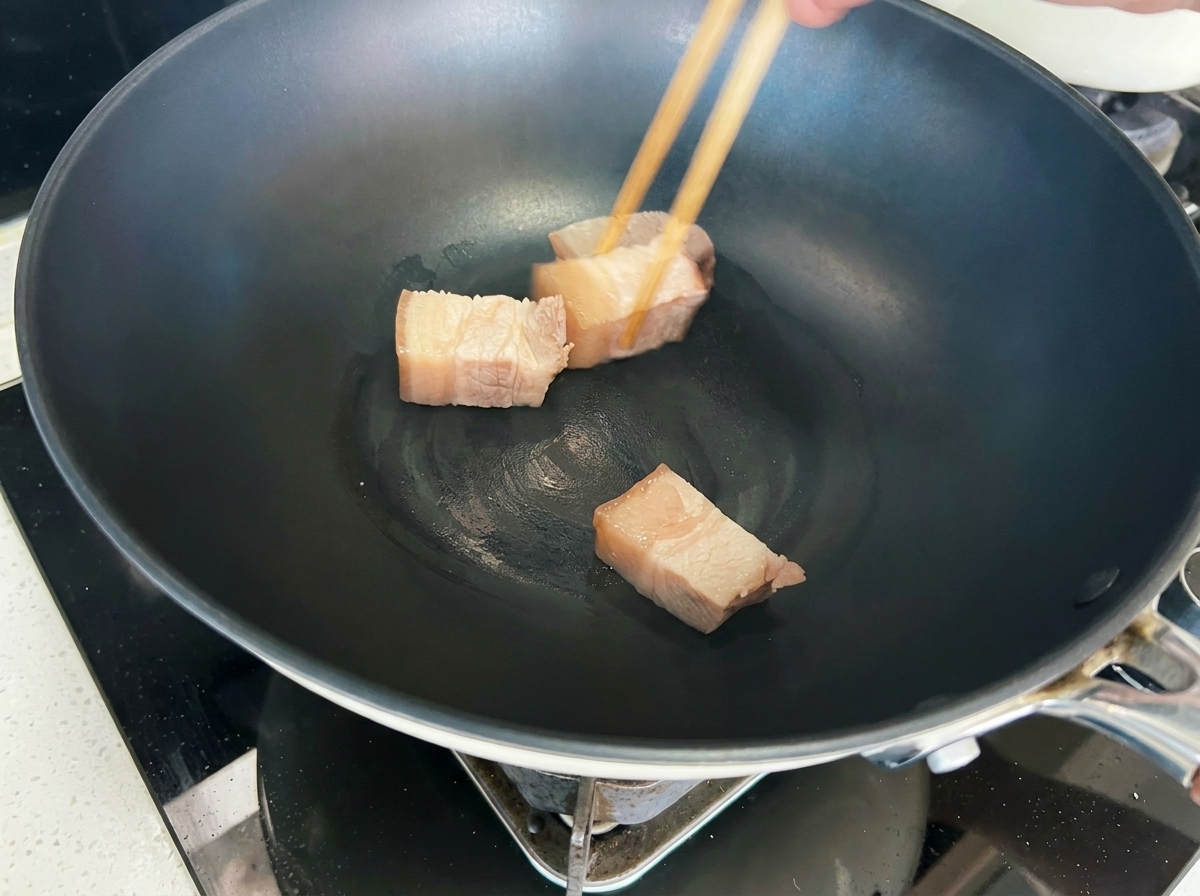 Pork cubes being seared in a wok until they turn a golden-brown color.