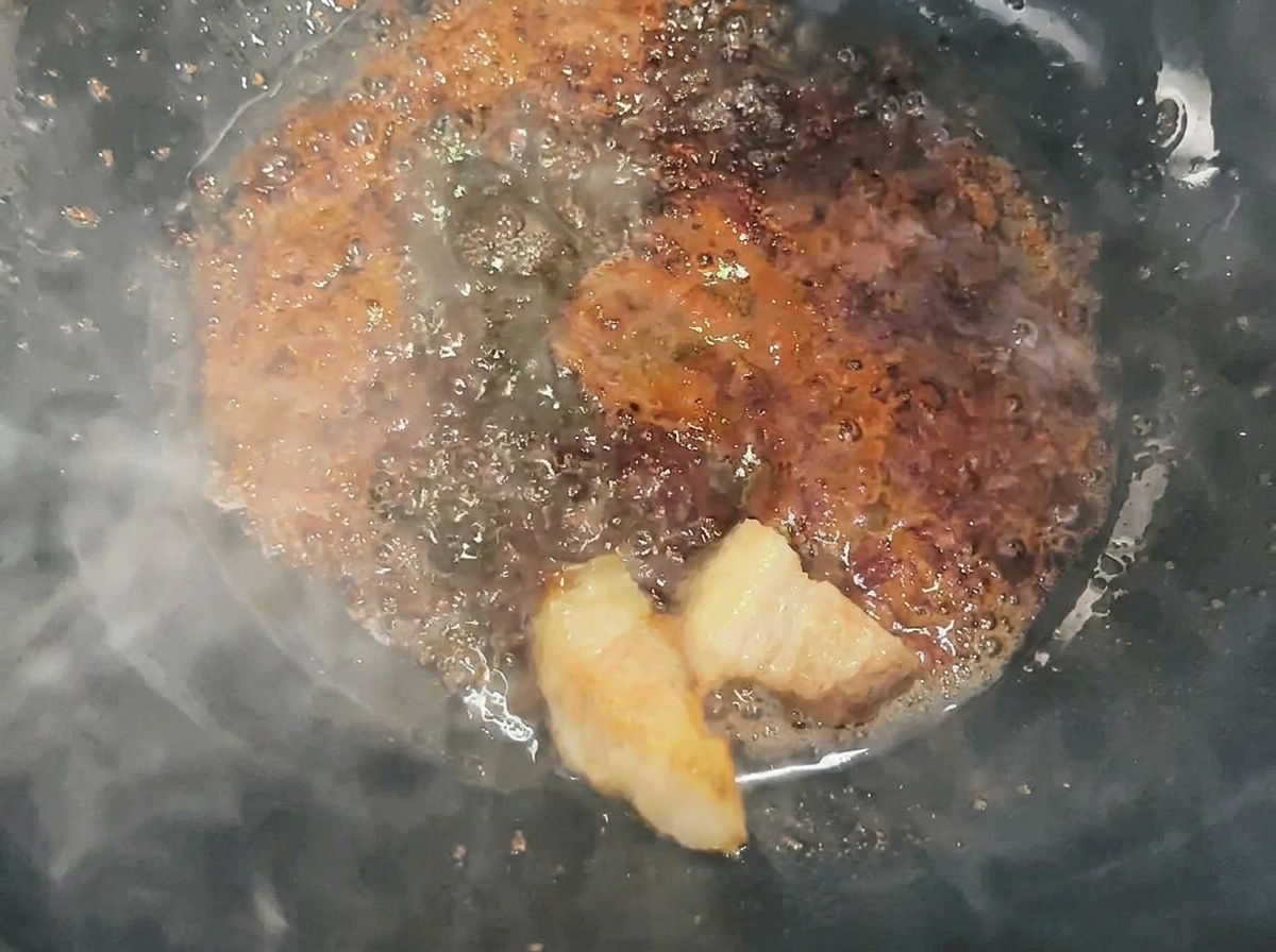 Pork cubes being tossed and coated in liquid caramel in a wok.