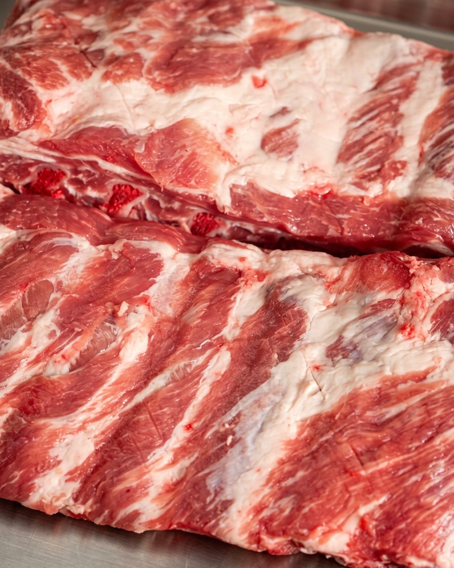 Red chili powder and dark spices being sprinkled onto the surface of scored raw pork ribs.